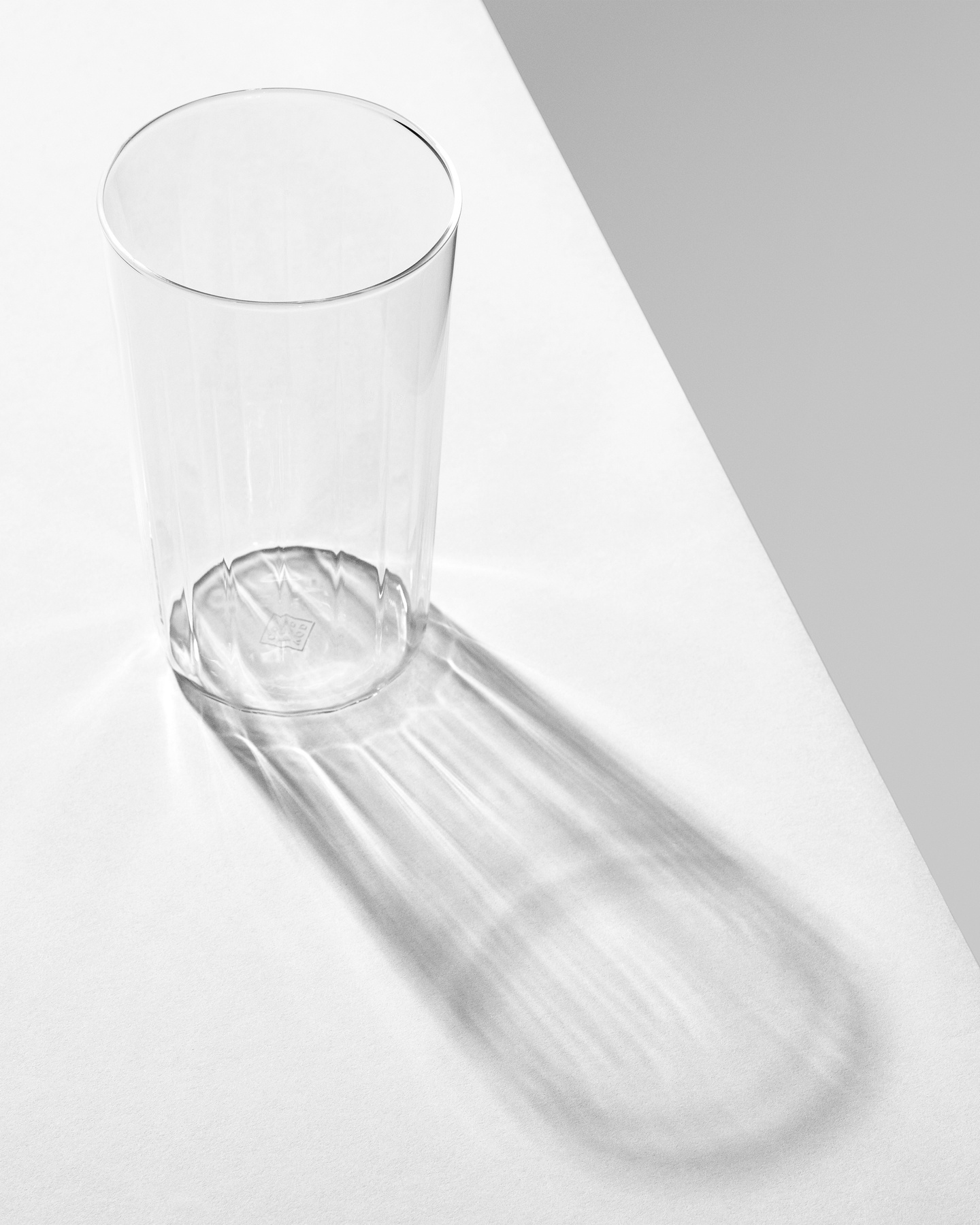 Tall clear glass tumbler casting shadow on a white surface