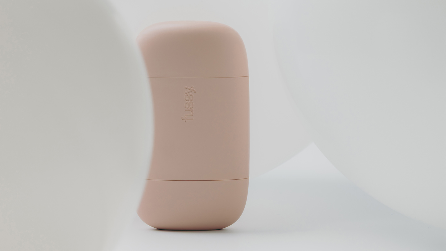 Pink Fussy refillable deodorant case standing upright between white smooth shapes.