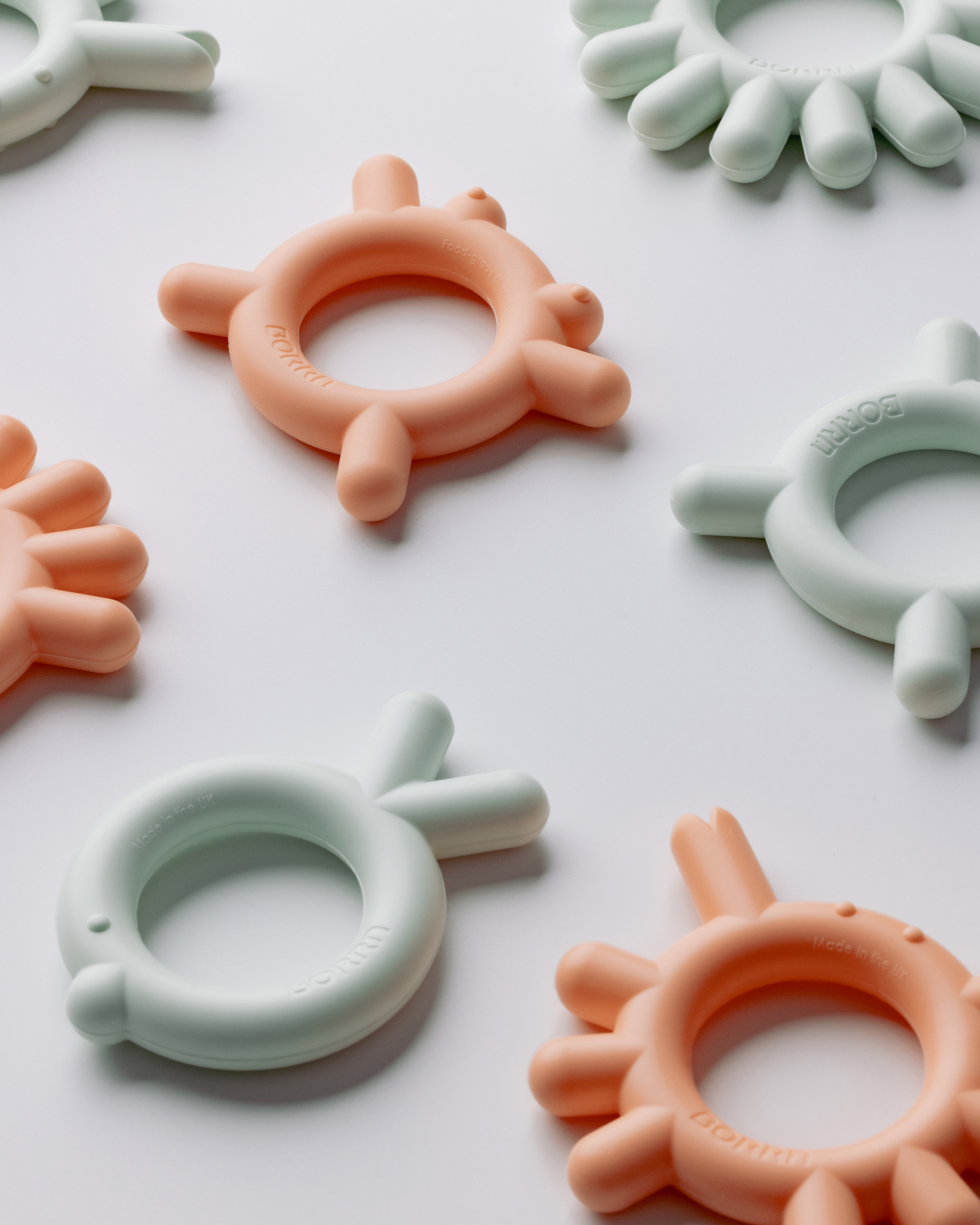 Angled shot of several peach and green coloured teethers on a light background.