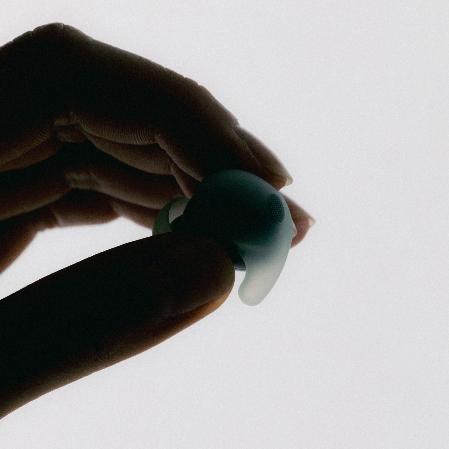 Hand holding a small translucent light-blue soft object against a pale background