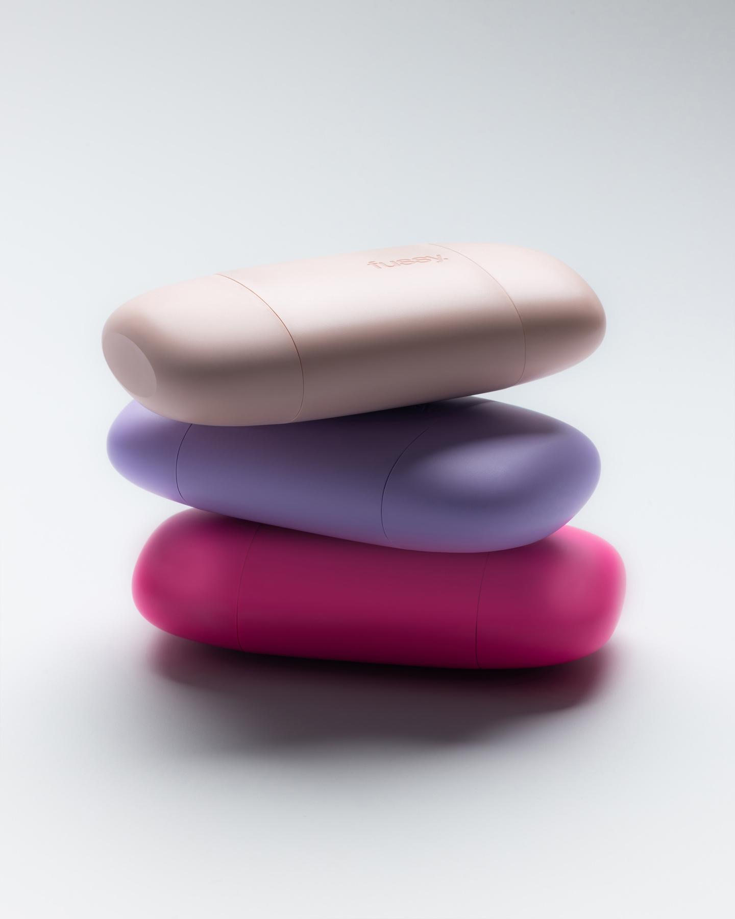 Three pebble-shaped Fussy deodorant cases in shades of pink and purple stacked up.