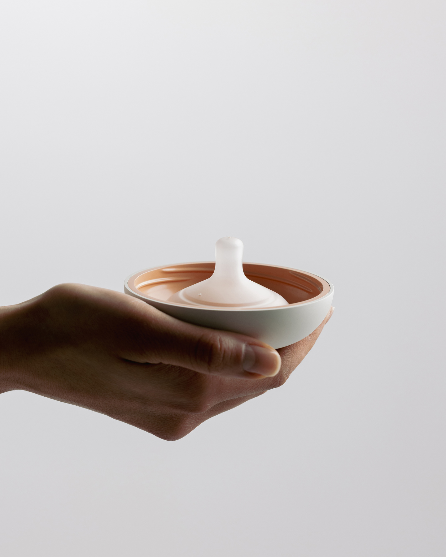 Hand holding a translucent shell component of the Avira breast pump.