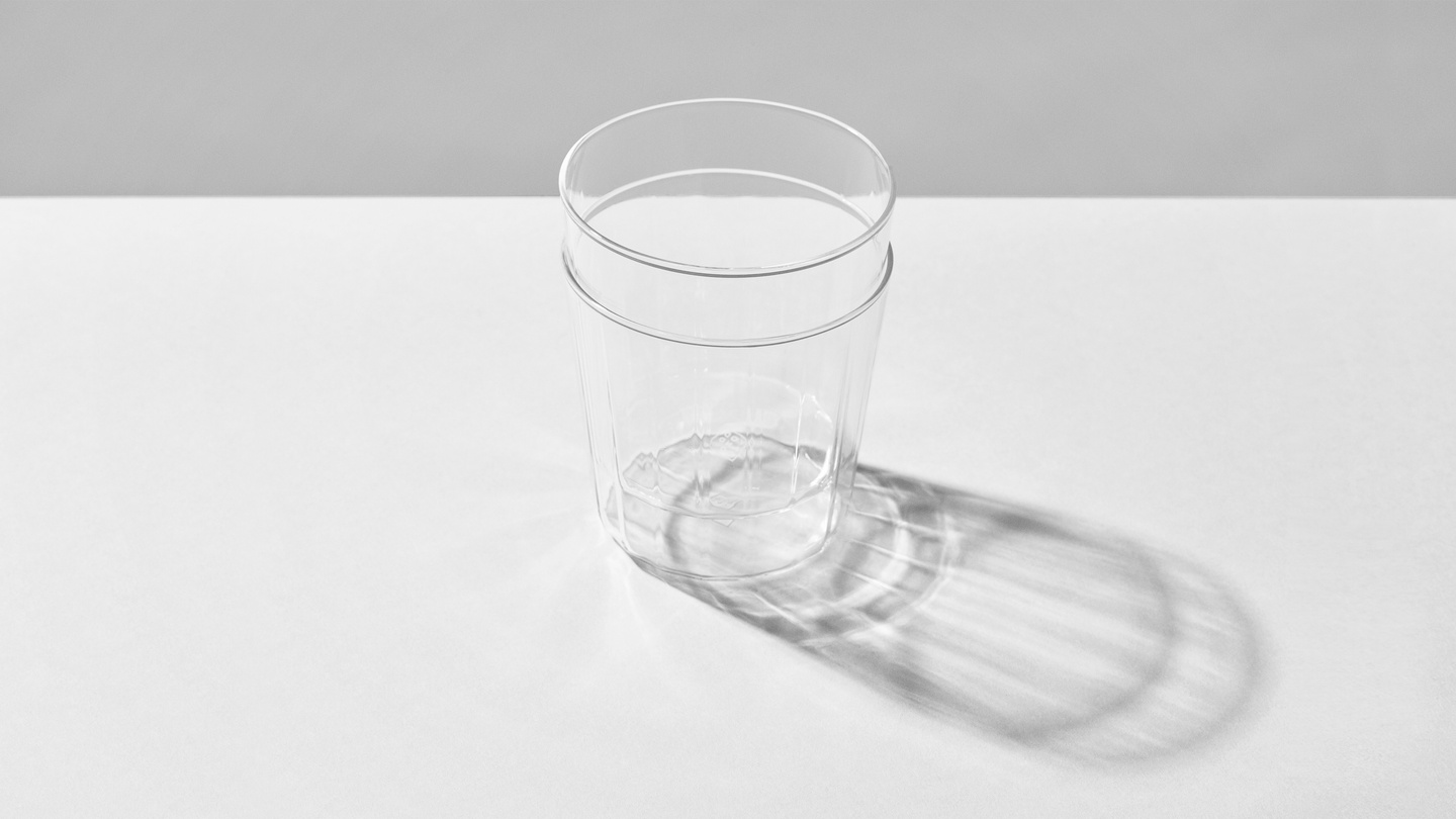Two stacked clear glass tumblers casting light shadows on a white surface