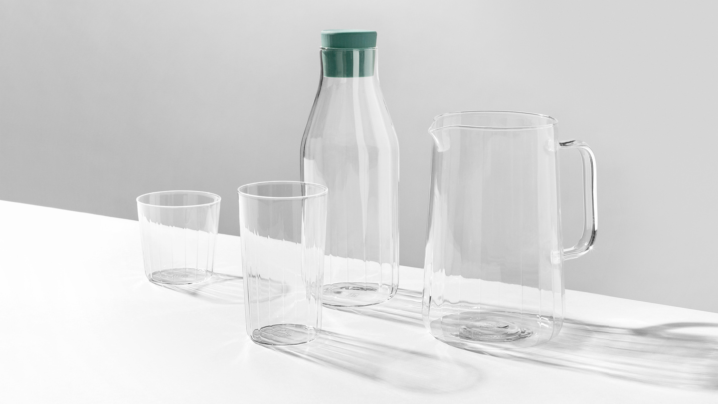 Clear glass carafe with green lid next to a glass pitcher and tumbler on a white surface