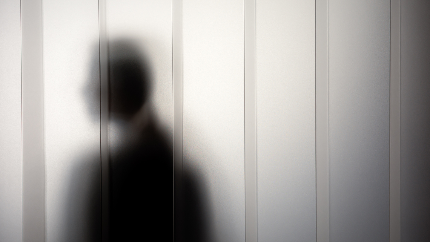 Person standing behind semi-translucent white curtain panel