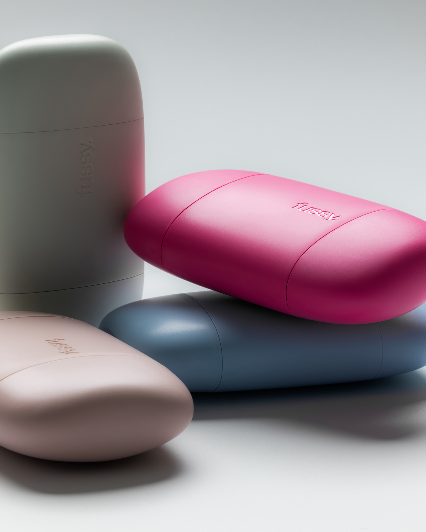 Close-up of pink, light grey, and blue Fussy deodorant cases stacked together.