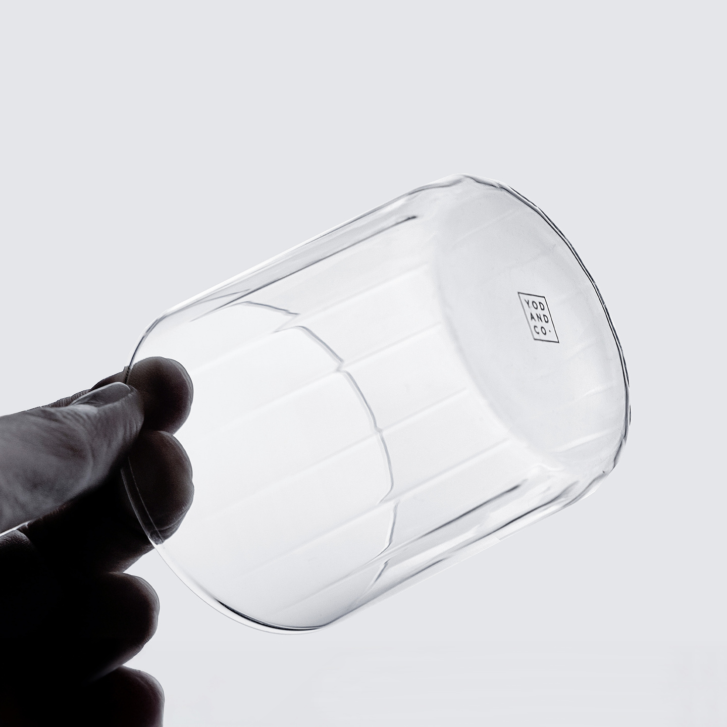 Hand holding a transparent glass tumbler against a white background