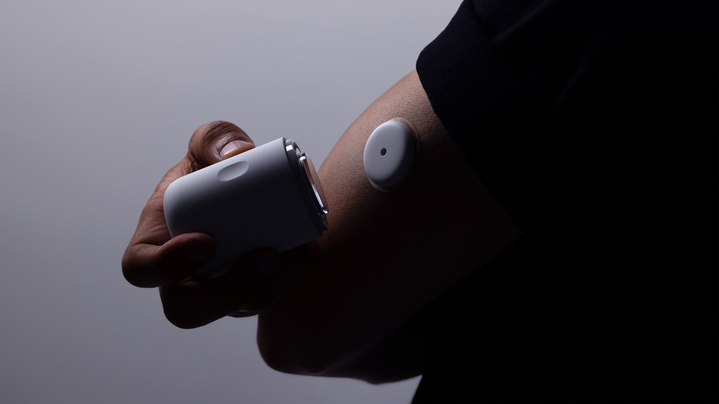 Person using a white applicator to apply a circular continuous glucose monitor sensor onto their upper arm