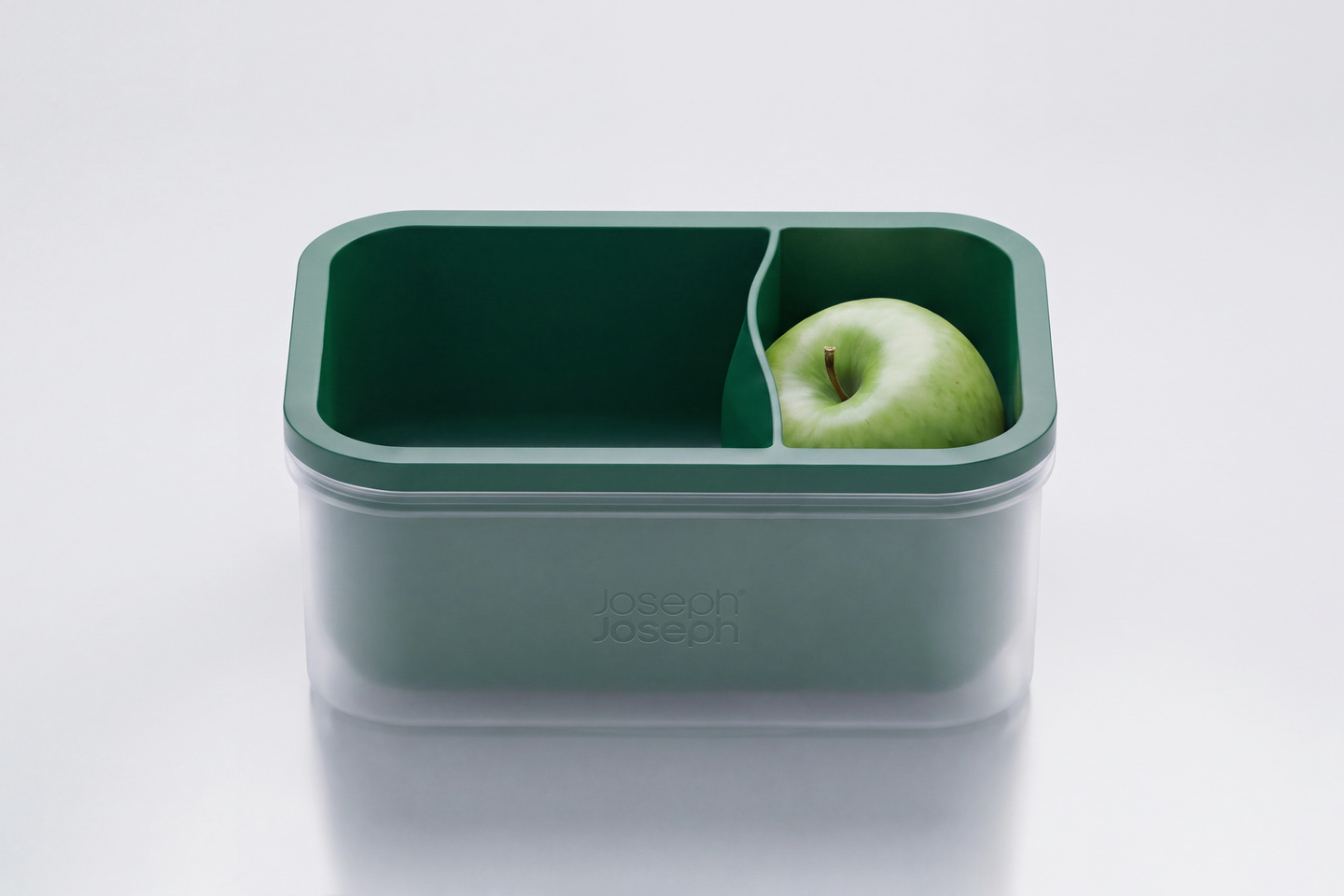 Green compartment lunchbox container holding a green apple on a white surface