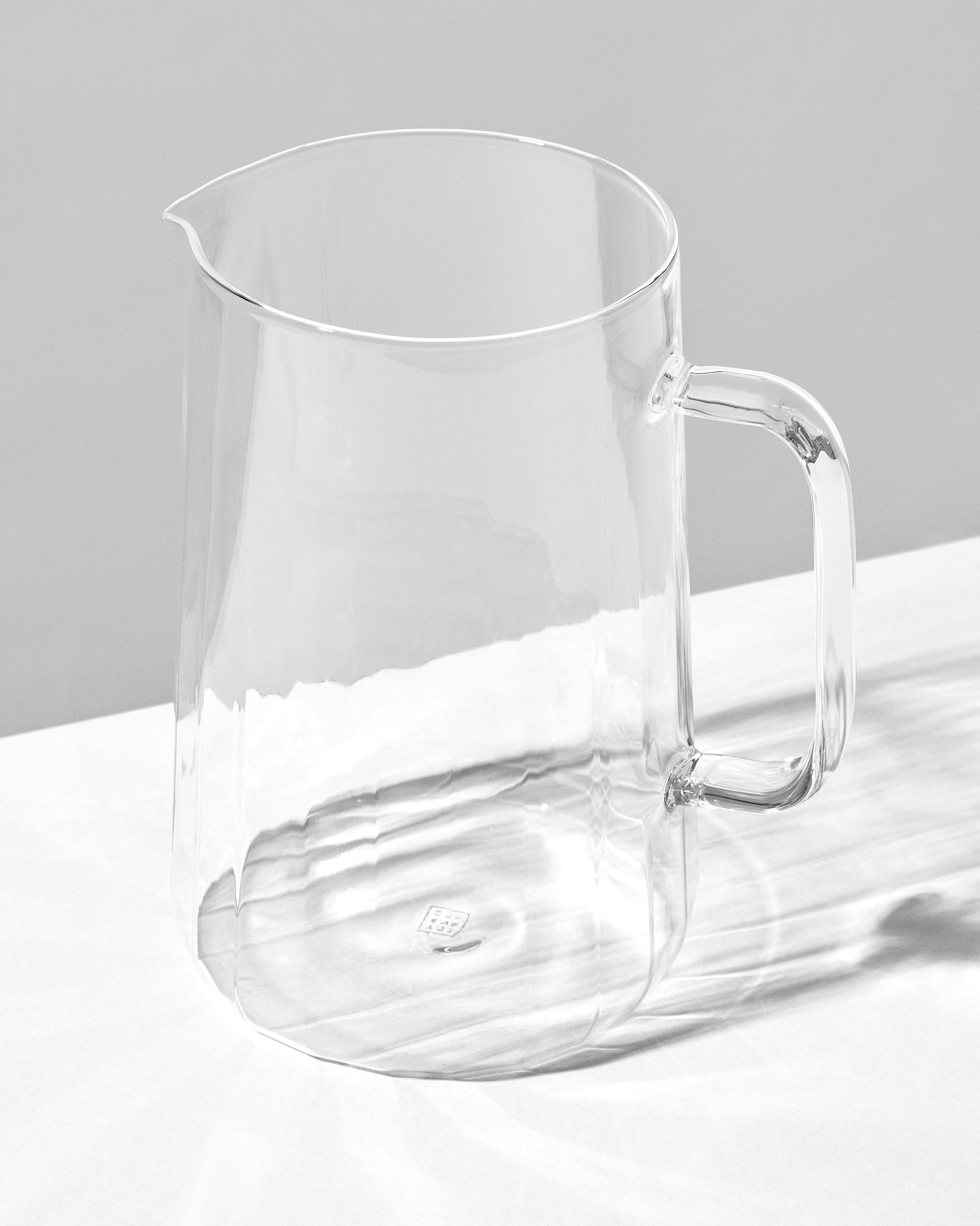 Clear glass pitcher with handle standing on a white surface