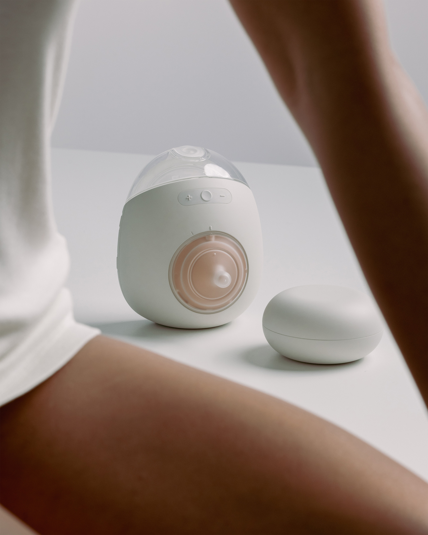 Seated woman with the Avira breast pump resting on a surface in the background.