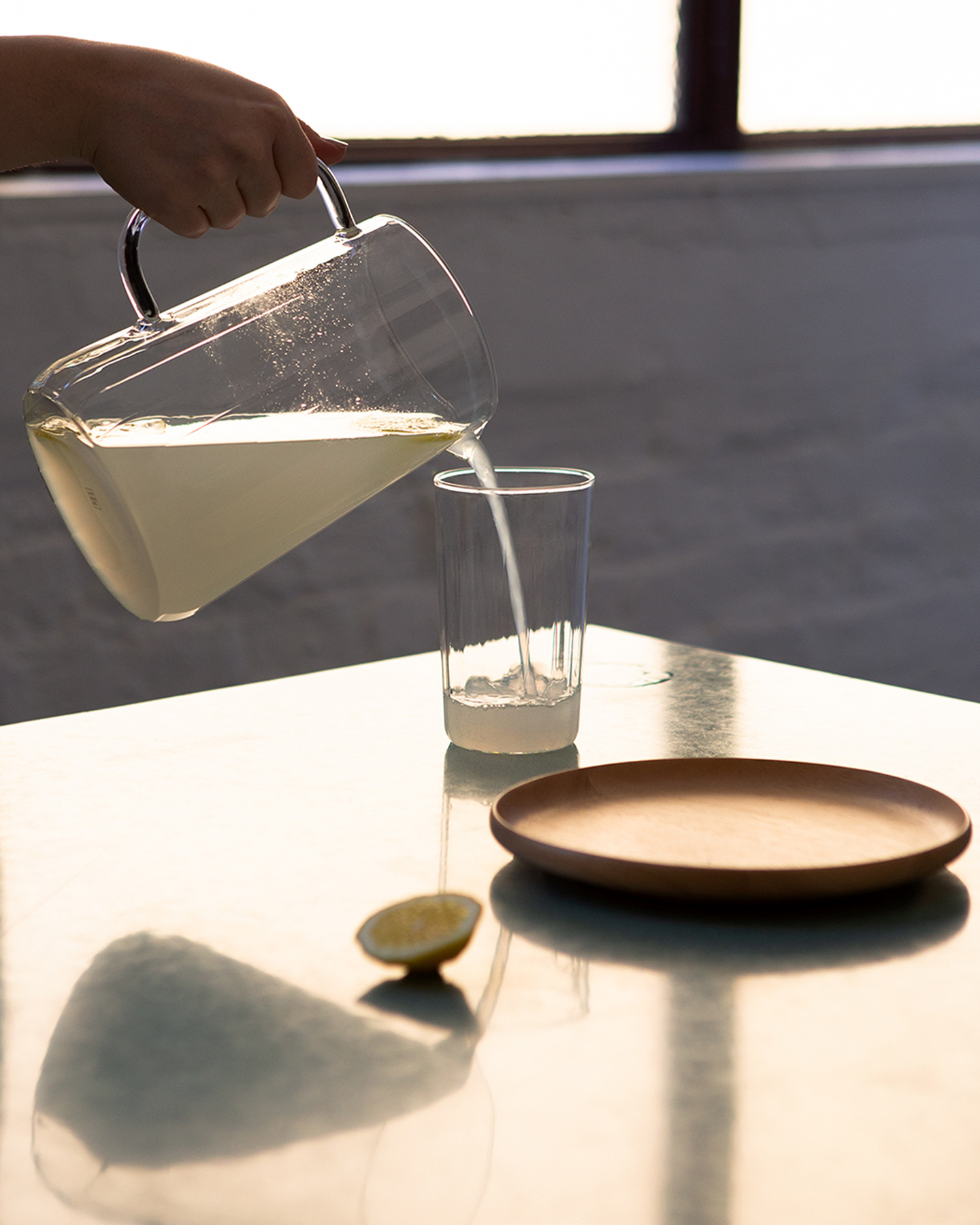 Person pouring water from a glass pitcher into a glass tumbler