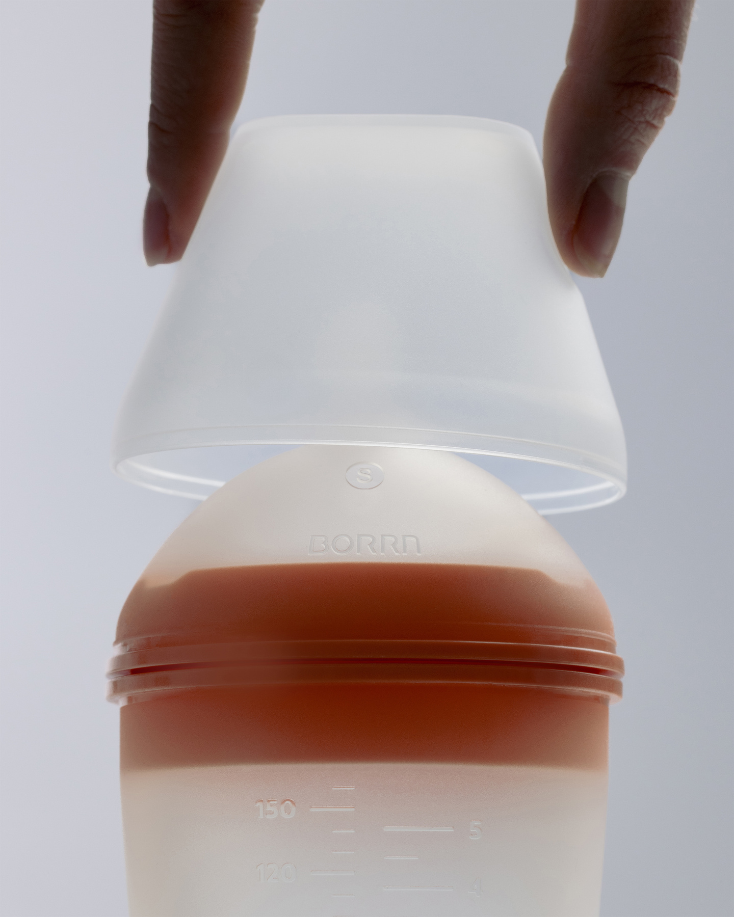 Close-up of hand remove cap from translucent silicone baby feeding bottle.