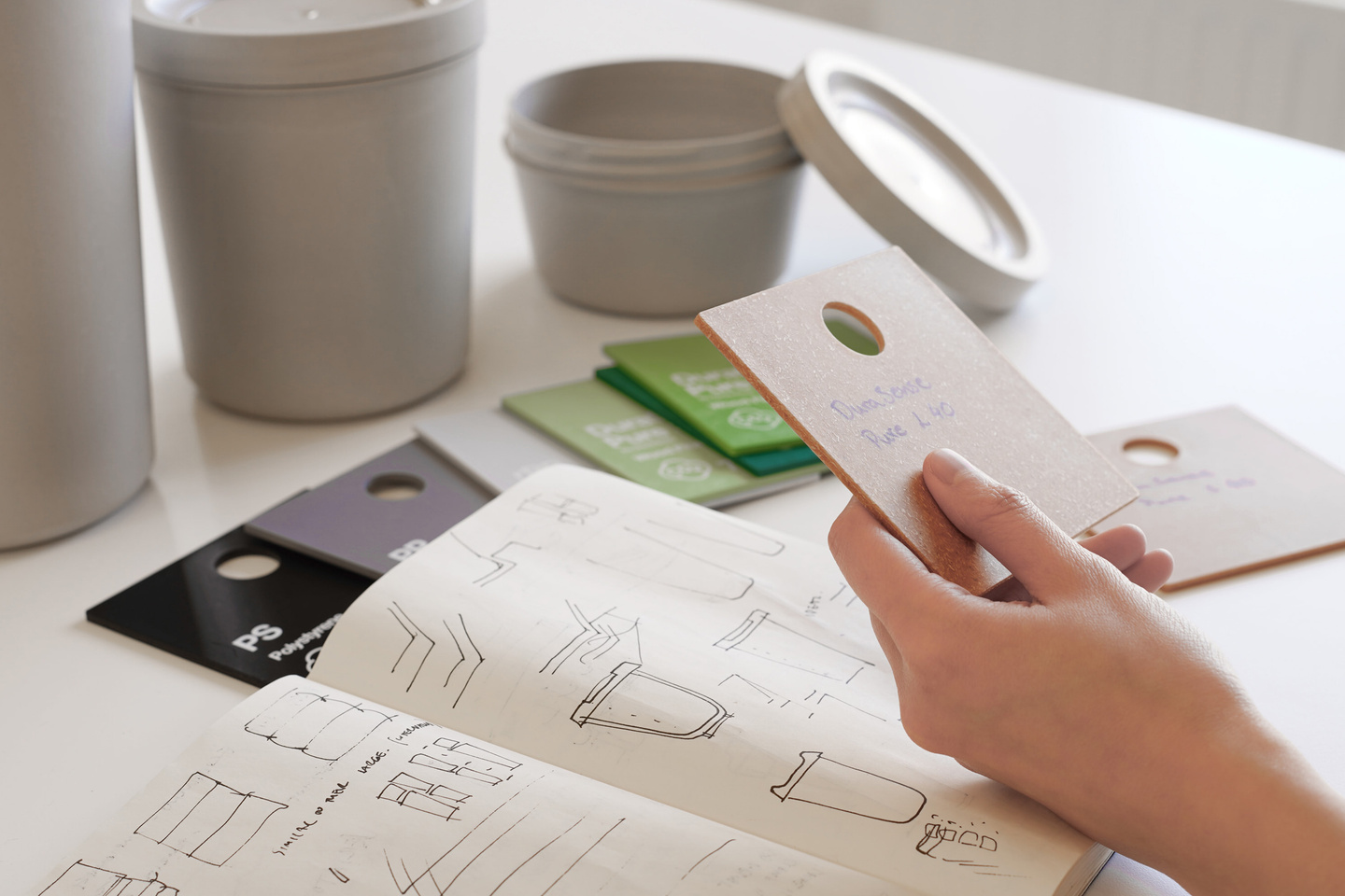 Hand holding a colour reference book next to reusable packaging containers.