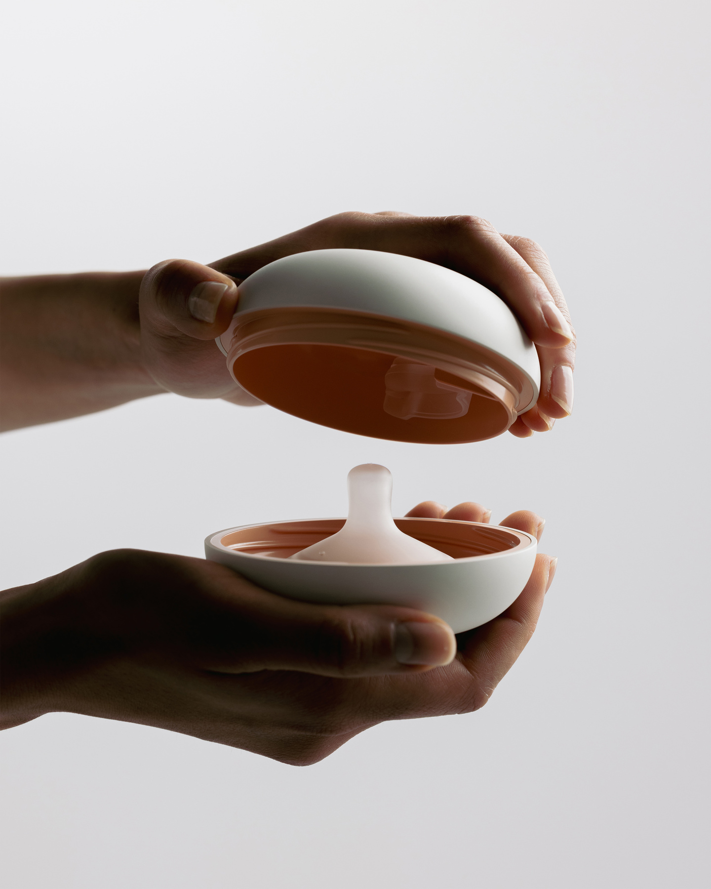 Hands holding and opening the two halves of the Avira breast pump outer shell.