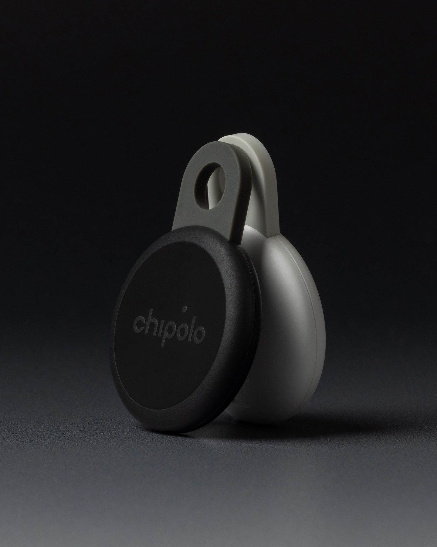 Studio shot of a black circular Chipolo Loop tracker standing on a dark surface.