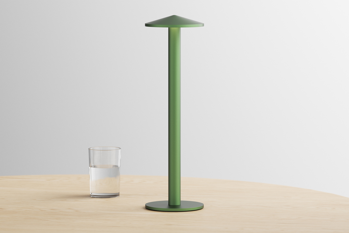 Green Parasol Lamp standing next to a water glass on a wooden table.