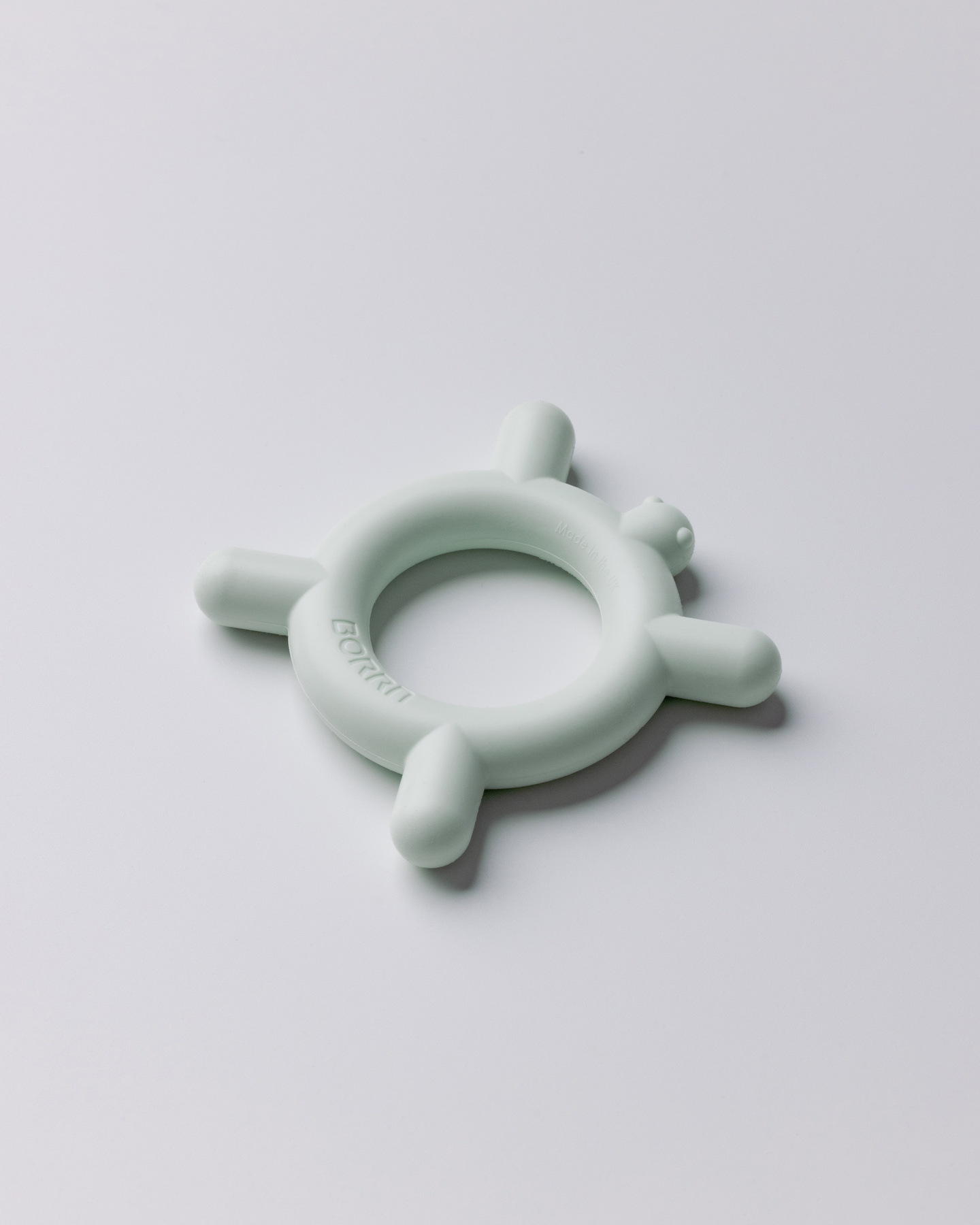 Distance view of green-coloured circular silicone teether ring shown on a light background.