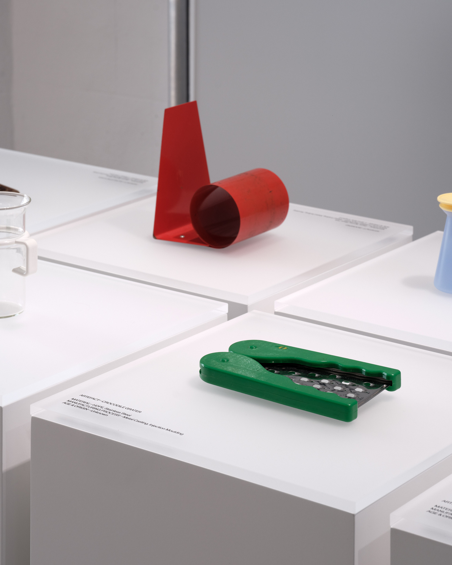 Close up of objects on white plinths in front of white panelled scaffolding wall