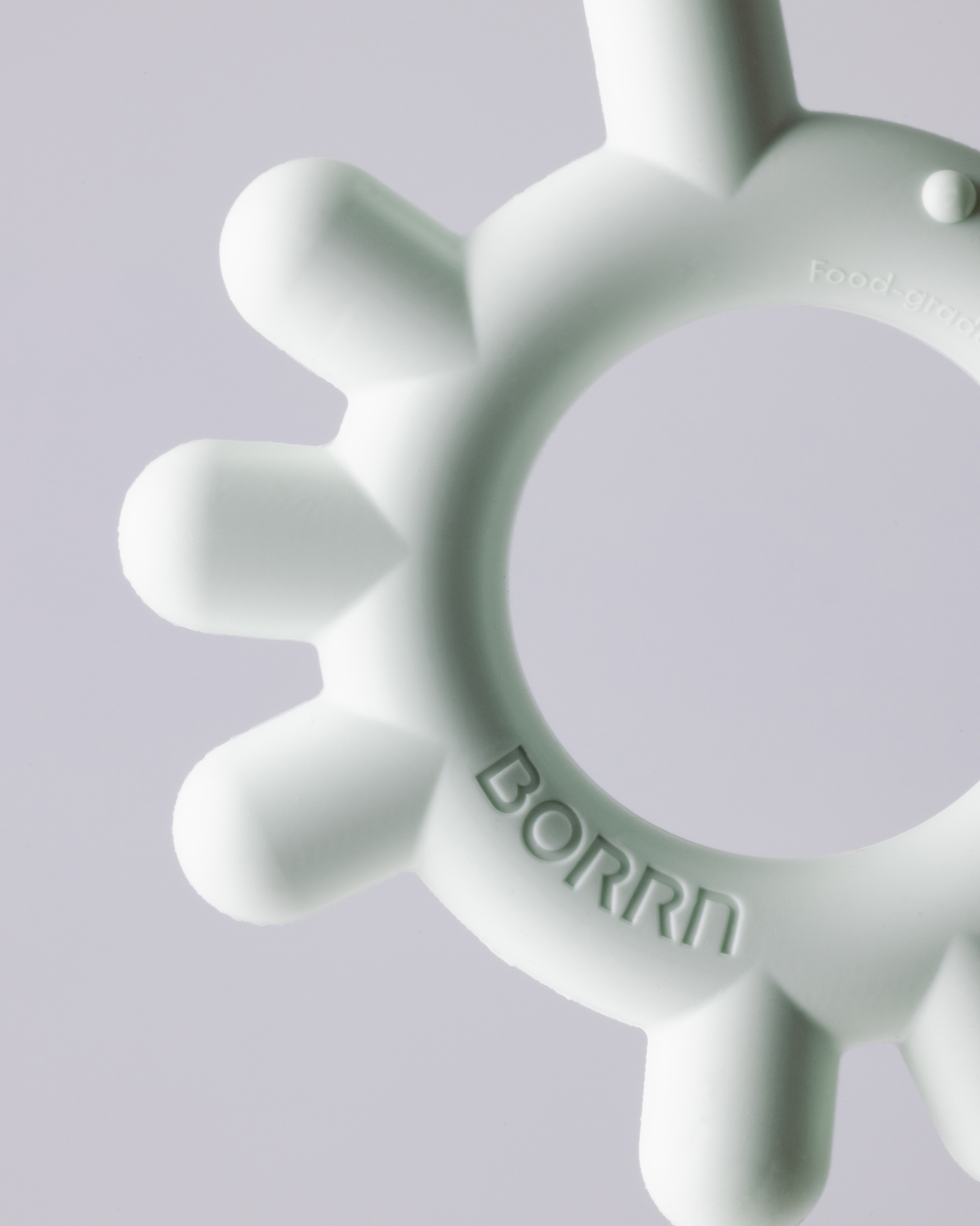 Cropped detail shot of green-coloured circular silicone teether ring on a light background.