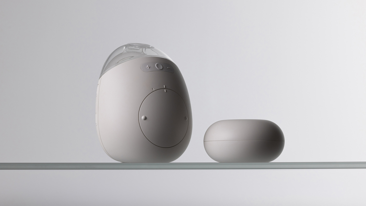 Studio shot of the Avira breast pump unit standing next to its charging base.